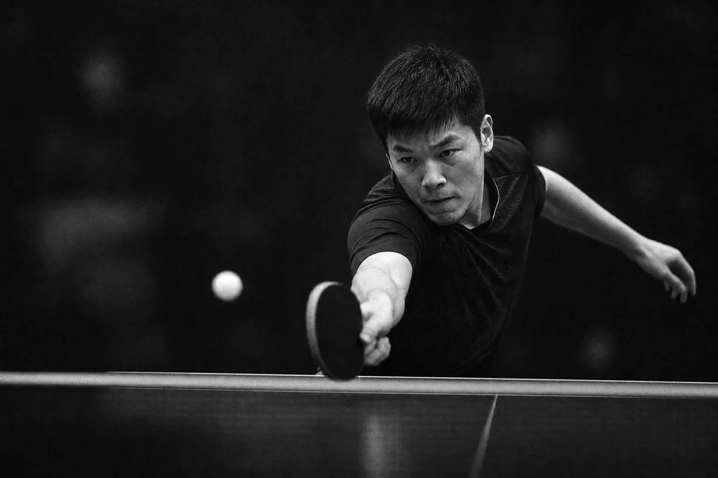 Table tennis player reaching for a forehand under a spotlight