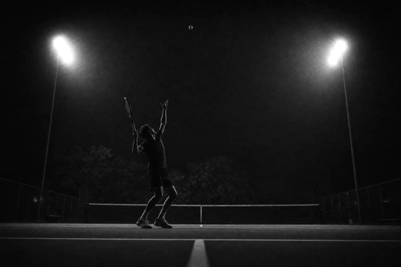 Tennis player serving on a floodlit court at night